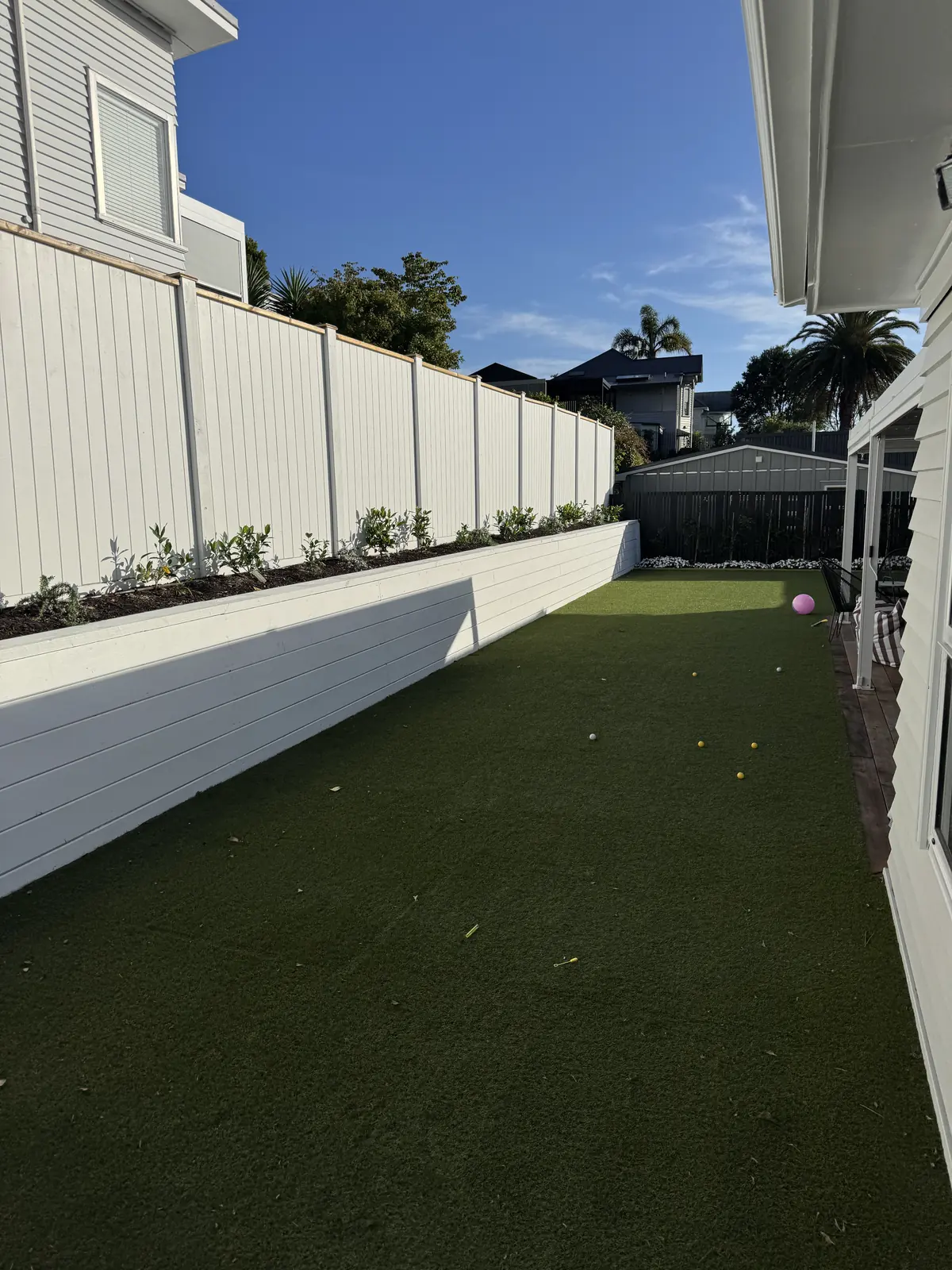 The same side yard after, with a raised garden bed along a white wall and clear turf