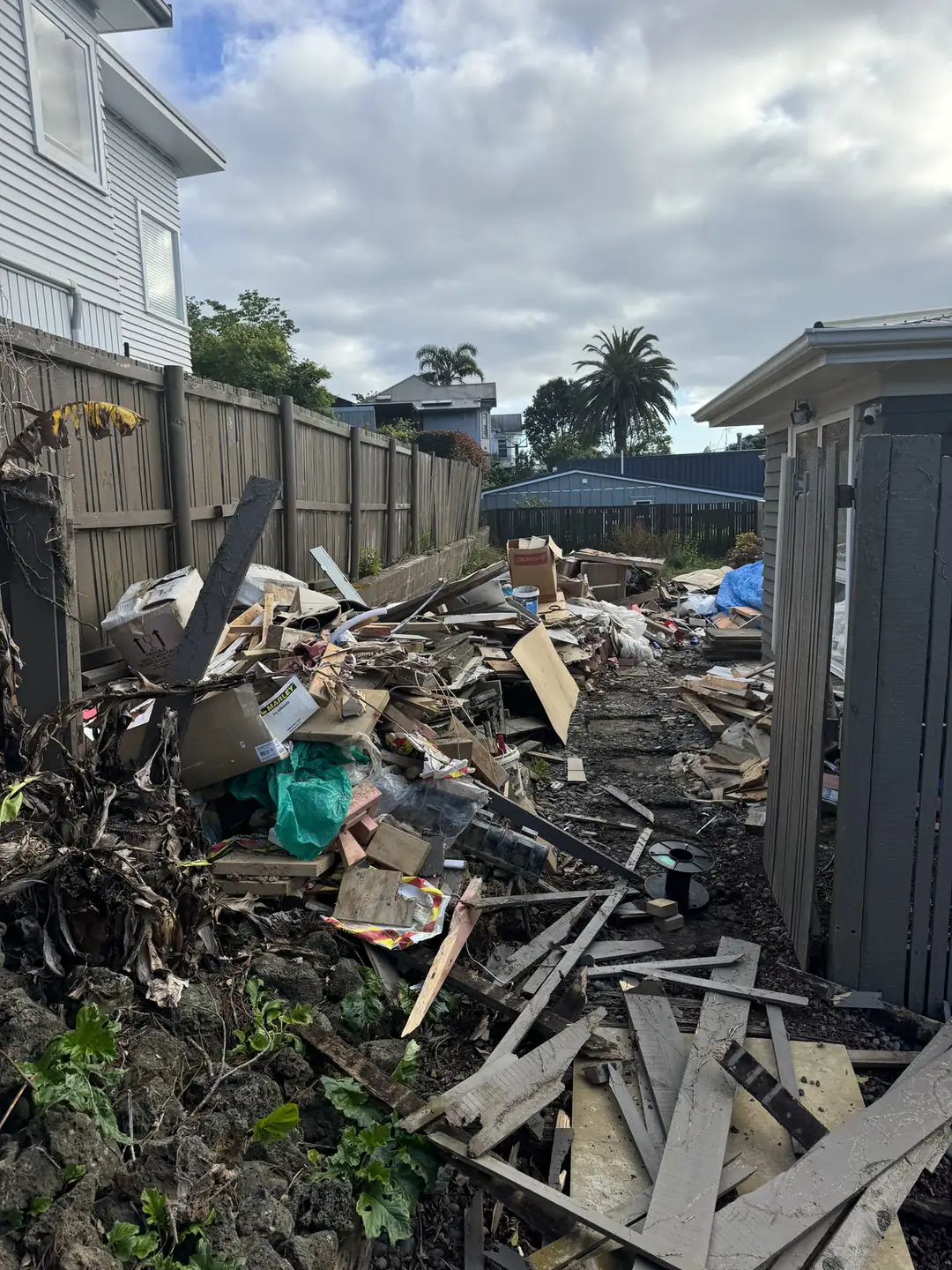 Side yard buried in timber offcuts, cardboard and building debris before the clean-up