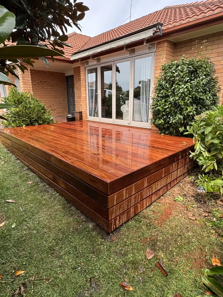Raised timber deck with a stepped edge in front of glass doors on a brick home