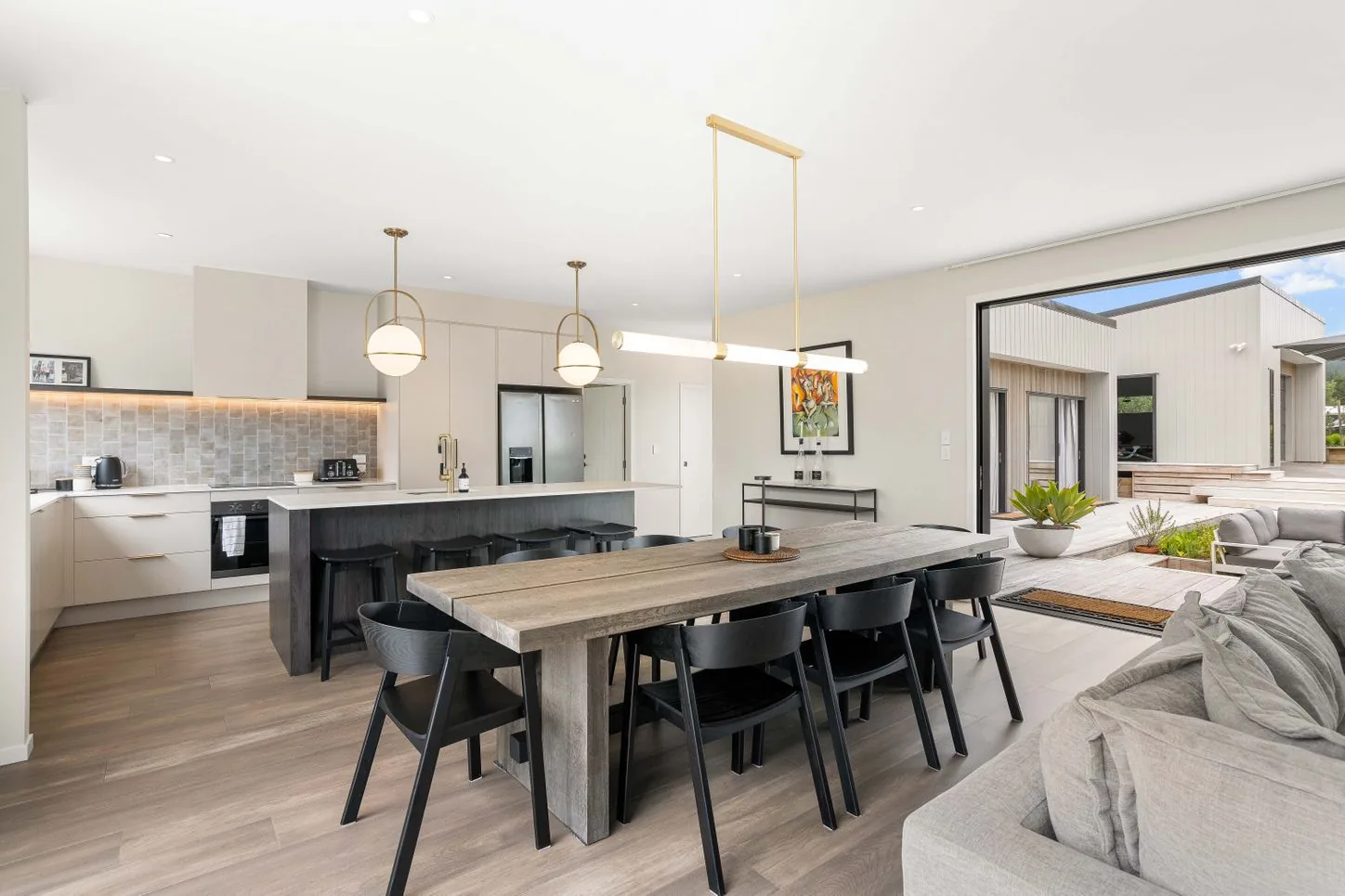 Kitchen with a dark island, black stools and brass pendant lights
