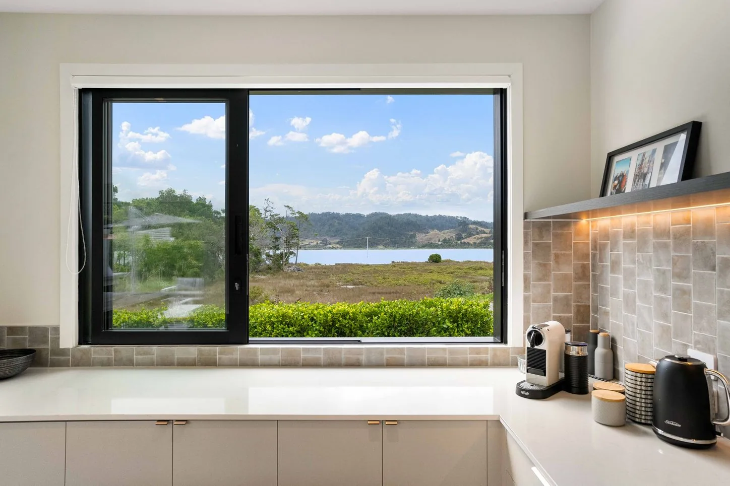 Kitchen window above a pale benchtop with tiled splashback and an under-shelf light