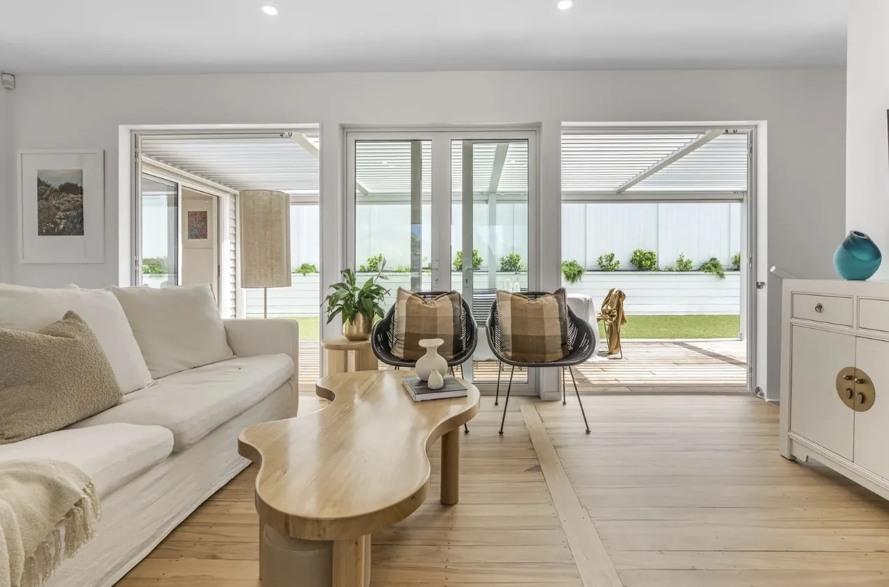 Living room with a white sofa, a curved timber coffee table and glass doors to a covered courtyard
