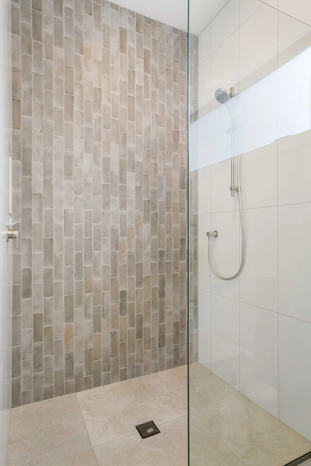 Walk-in shower with a vertical tiled feature wall, large white wall tiles and a glass screen
