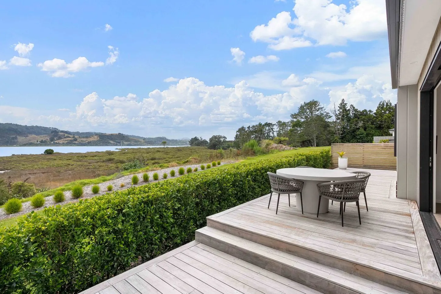 Timber deck steps beside a hedge with an estuary view
