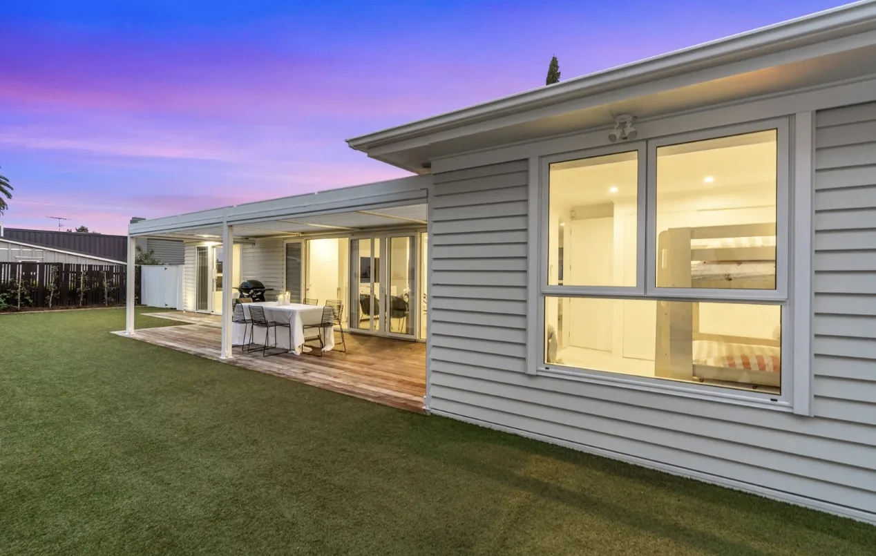 Side of a weatherboard house with a pergola at dusk